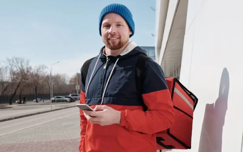 Man in casual wear holding phone, ready for delivery on sunny day.