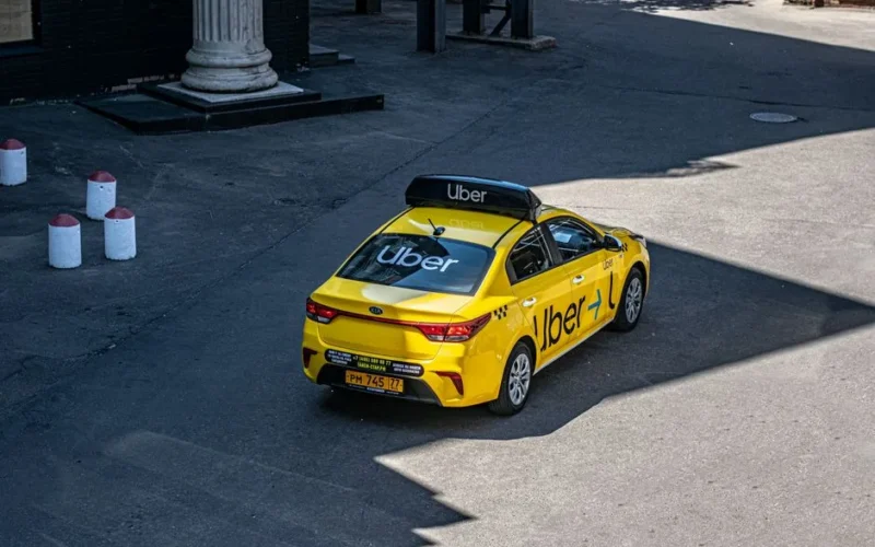 A yellow Uber taxi driving on a city street, shown from above.
