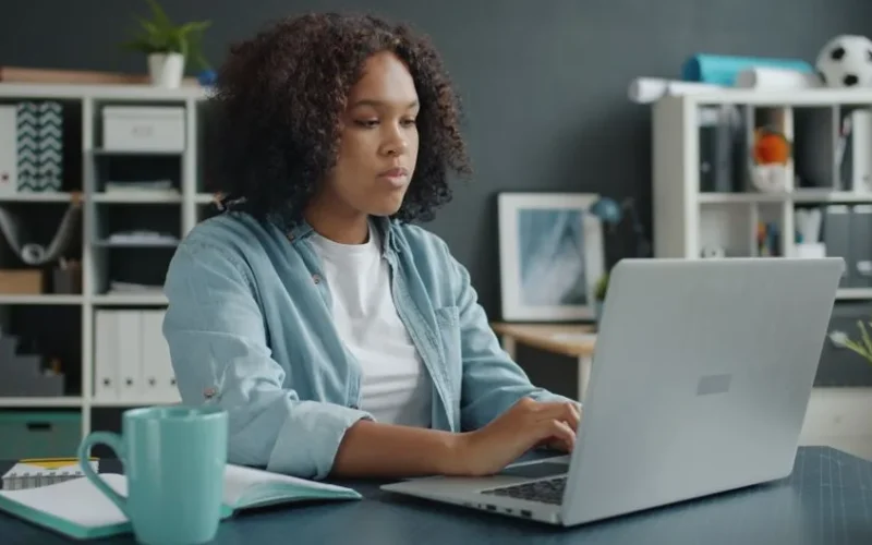 Young woman focused on remote work at home office desk with laptop.