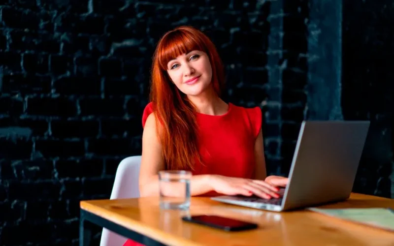 Redheaded woman in office working on a laptop, exuding professionalism and poise.