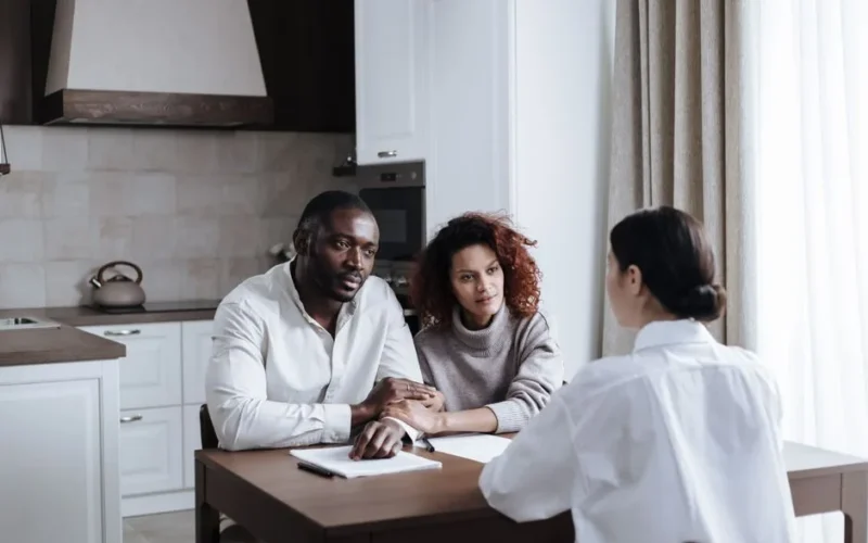 A couple discusses adoption with a social worker in a modern kitchen setting.