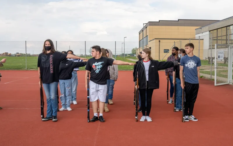 Spc. Garrett Nussbaumer, assigned to the 1st Battalion (General Support), 214th Aviation Regiment, guides JROTC cadets on the courts at Ansbach Middle High School, Germany, May 2, 2022. Nussbaumer has been volunteering his time to assist the JROTC drill team, which recently wrapped up their season and finished second place in the Department of Defense Education Activity Army JROTC European Championship. 12 CAB is among other units assigned to V Corps, America's Forward Deployed Corps in Europe. They work alongside NATO Allies and regional security partners to provide combat-ready forces, execute joint and multinational training exercises, and retain command and control for all rotational and assigned units in the European Theater. (U.S. Army photo by Cpt. Gabrielle Hildebrand)
