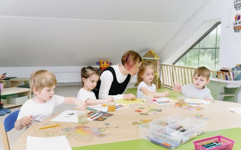 Young children engaging in art activities with a teacher in a bright kindergarten classroom.