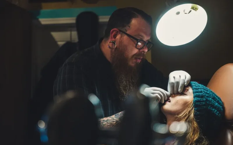 Professional piercer wearing gloves works on client in studio, focused on precision and detail.