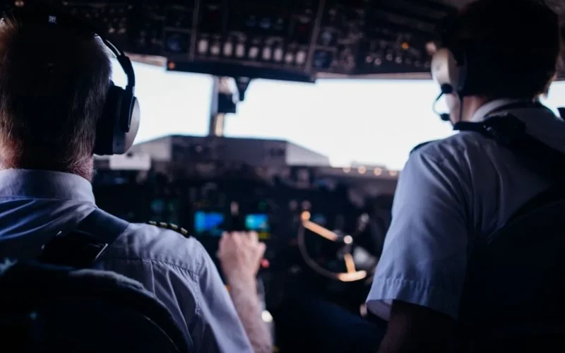 Back view of anonymous male pilots in uniform and headset navigating modern airplane while taking off
