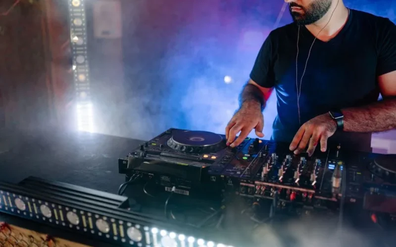 Energetic DJ performing live with mixing equipment in a colorful nightclub setting.