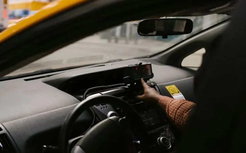 Anonymous ethnic male driver with steering wheel using GPS navigator to search direction for drive on street in city during work