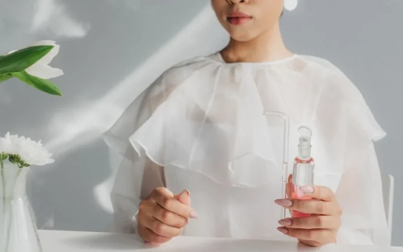 Woman in white blouse holding a glass flask in a minimalist laboratory environment.