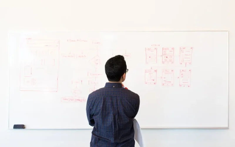 Man standing at a whiteboard planning UX design concepts in a modern office setting.