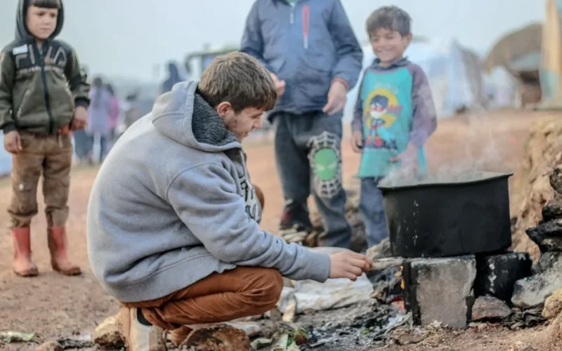 A group of children cooking over an outdoor stove at a refugee camp in Idlib, Syria.