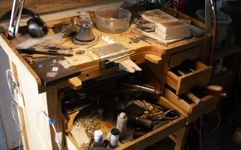 Jeweler's workbench for turning finished stones and other materials into custom pieces such as rings, pendants, bracelets, necklaces. Note the tool hanging at the upper right. This rotary cutting tool carves rock and stone with a cutting head attached to a flexible shaft. The speed of the tool can be controlled by hand or by a foot pedal.