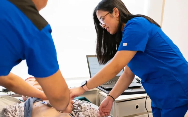 Nursing students practice using a medical mannequin in a simulation lab, focusing on patient care techniques.