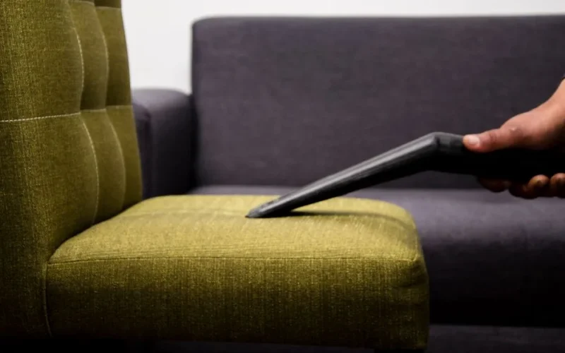 Close-up of a person vacuuming a modern sofa chair indoors, highlighting cleaning service.