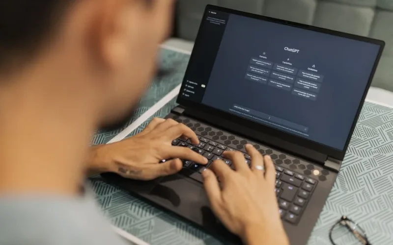 A focused individual types on a laptop running AI software indoors.