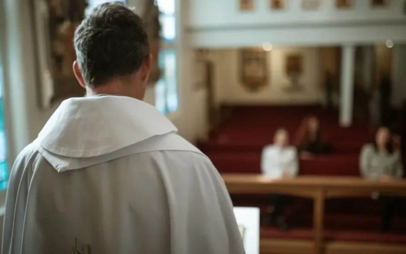 A priest immersed in reading the Bible while sitting in a church pew, capturing a serene spiritual moment.