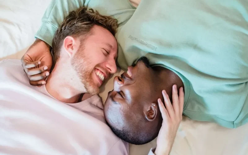 A joyful couple smiling and embracing while lying down together, showcasing love and comfort.