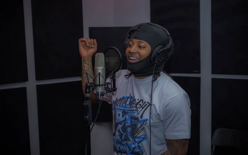Hip hop artist wearing a balaclava recording in a studio with a microphone.