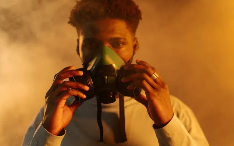 An adult man wearing a gas mask amidst smoke, emphasizing air pollution and protection themes.