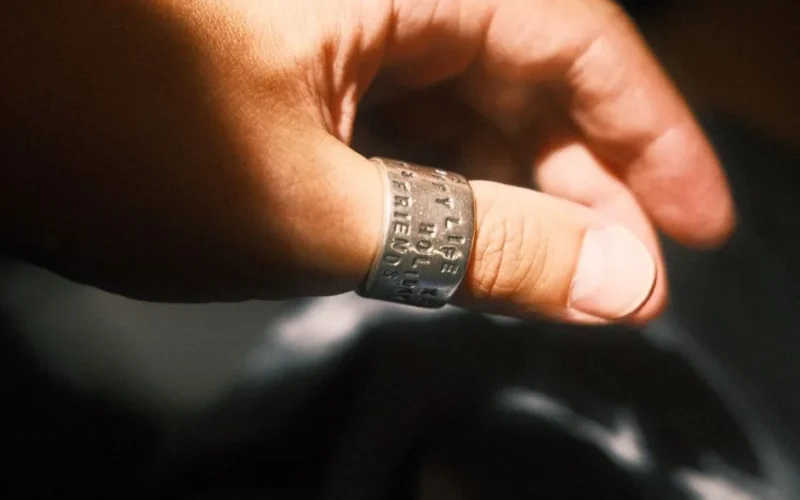 A close-up of a hand wearing an inscribed silver ring, captured in warm sunlight.