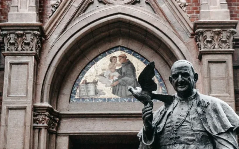 A statue of a pope holding a dove at a historic church entrance with beautiful archway.