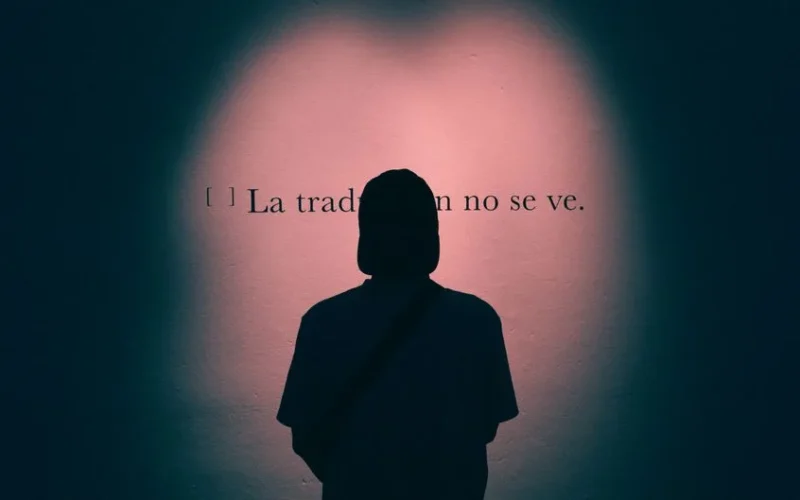 A silhouette of a man with a cap reading a Spanish quote on a pink-lit wall.