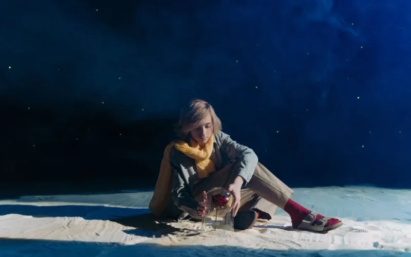 A young person in cosplay sits in a dreamy, starry setting with sand and roses.