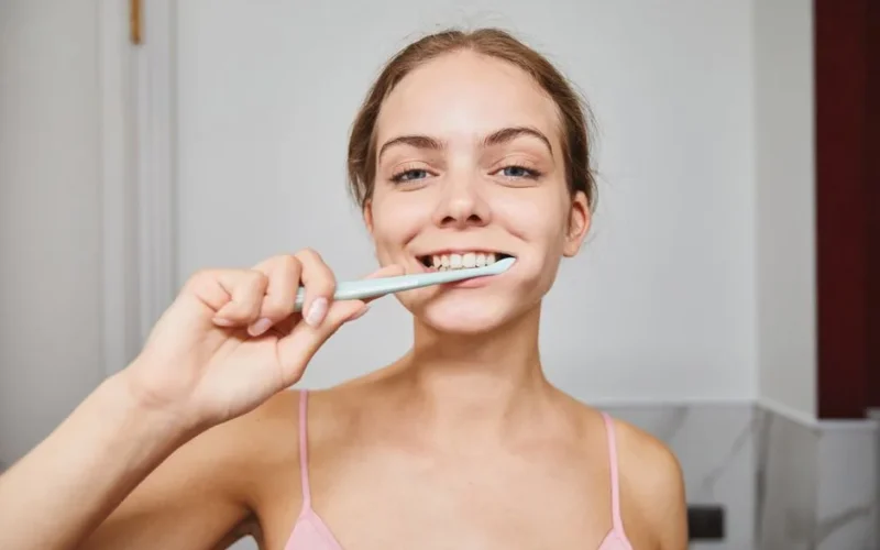Close-up of a woman smiling while brushing teeth in a modern bathroom.