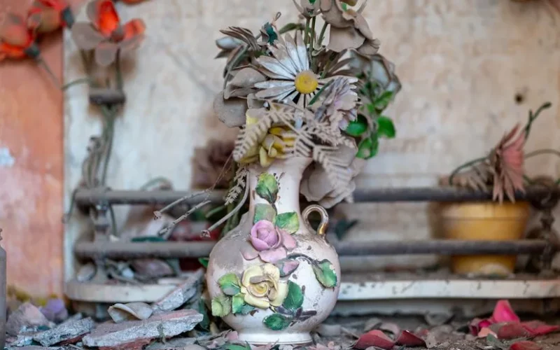 A detailed view of a vintage vase filled with dusty artificial flowers inside a cemetery in Punta del Agua, Argentina.