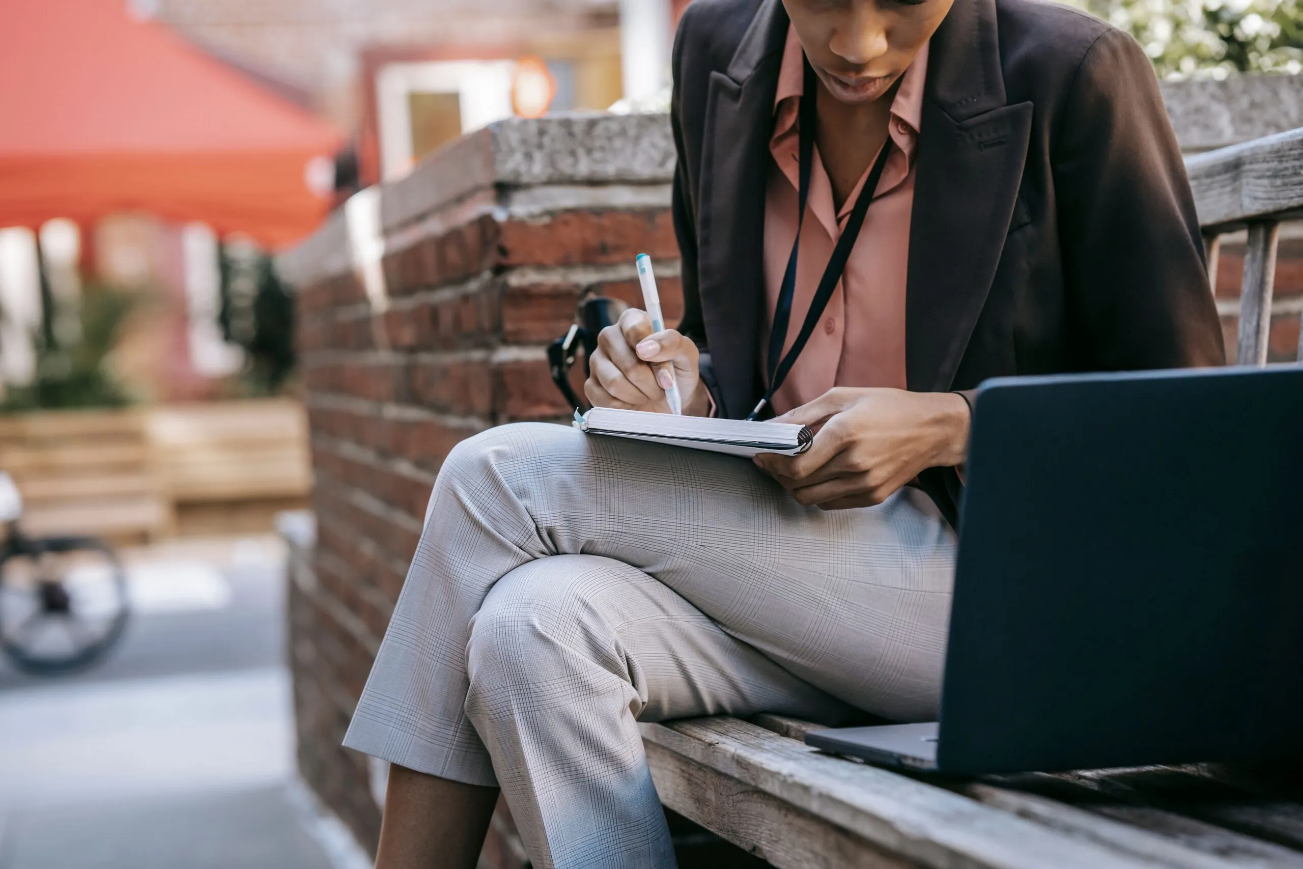 Crop anonymous African American female employee taking notes and using laptop while working on project