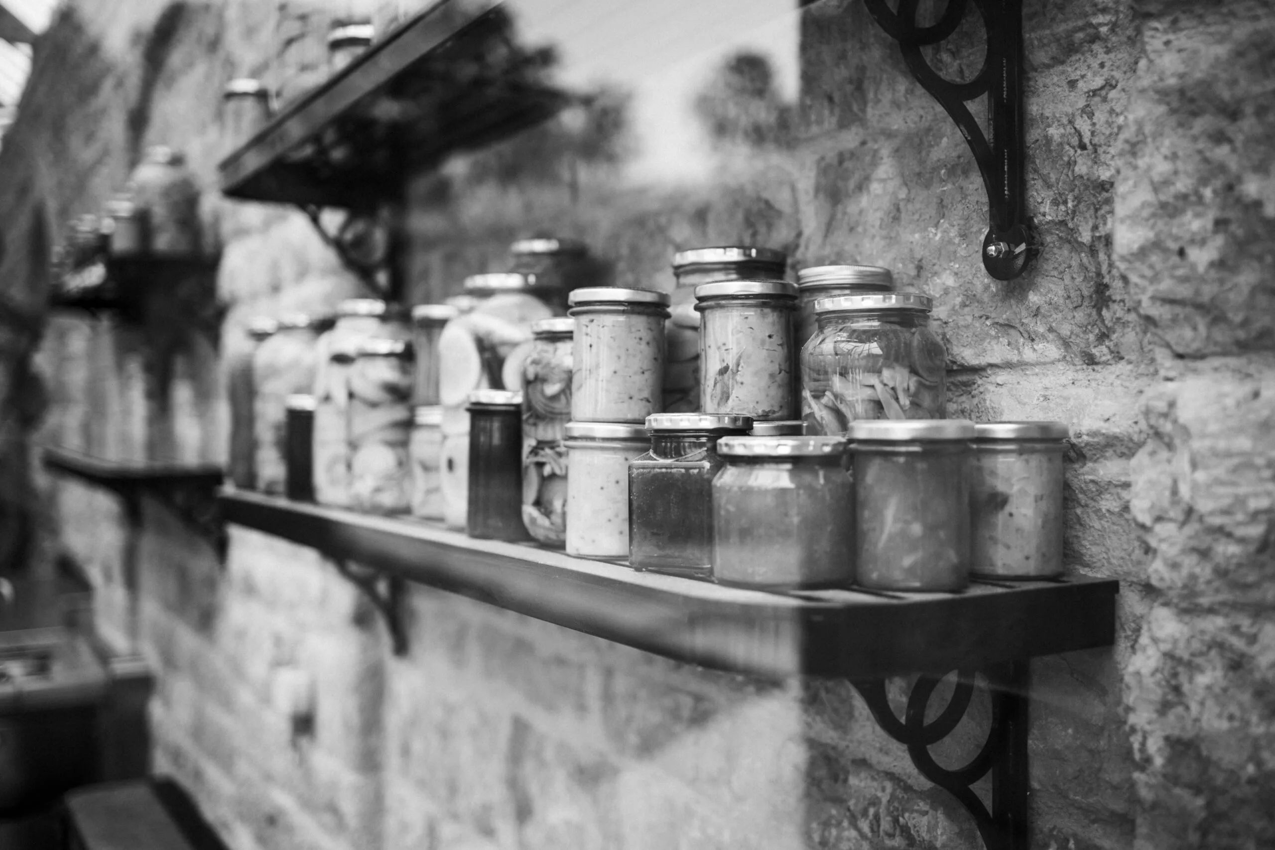 Black and white image of glass jars on rustic shelves indoors.