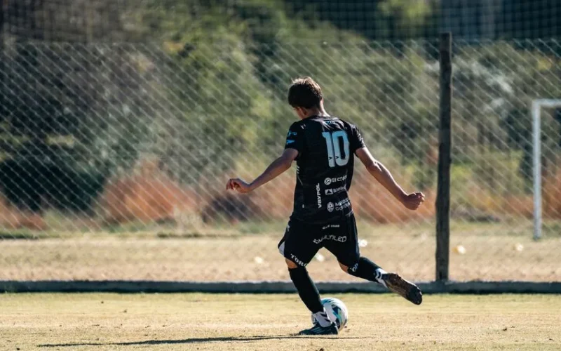 Young soccer player in black jersey with number 10 kicking a ball during a game on a sunny outdoor field.