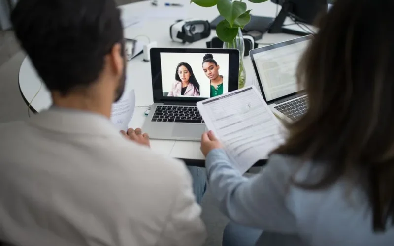 Two professionals conduct a virtual job interview using laptops in a modern office.