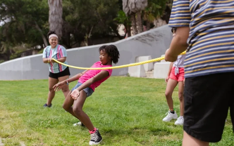 Children enjoy a fun limbo game on the grass at summer camp, promoting friendship and teamwork.