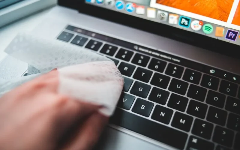 Person cleaning a laptop keyboard using disinfectant wipes for hygiene.