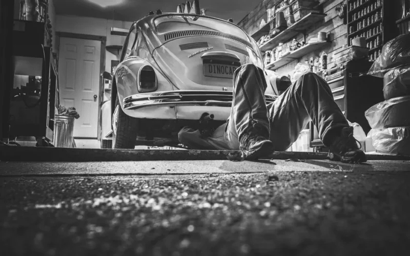 Mechanic working beneath a classic Volkswagen Beetle in a vintage garage setting.