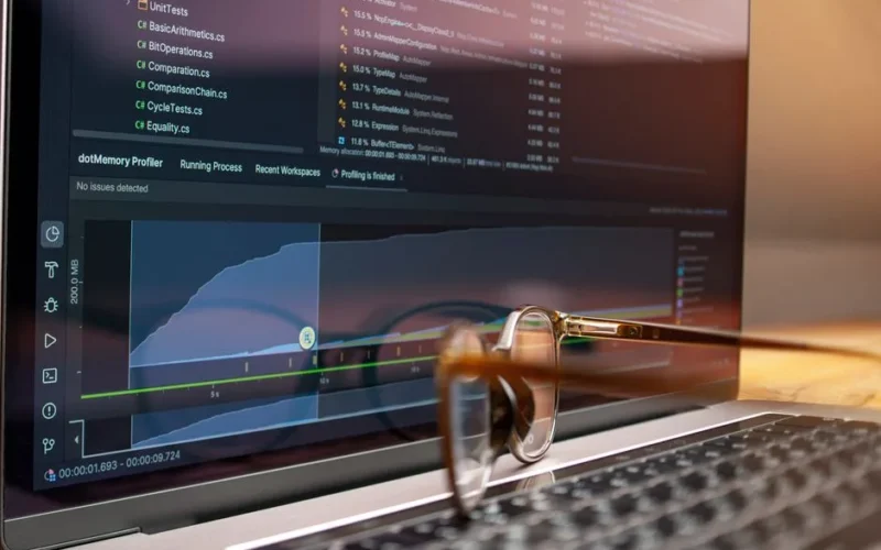 Laptop screen displaying code and performance graphs with eyeglasses resting on the keyboard.