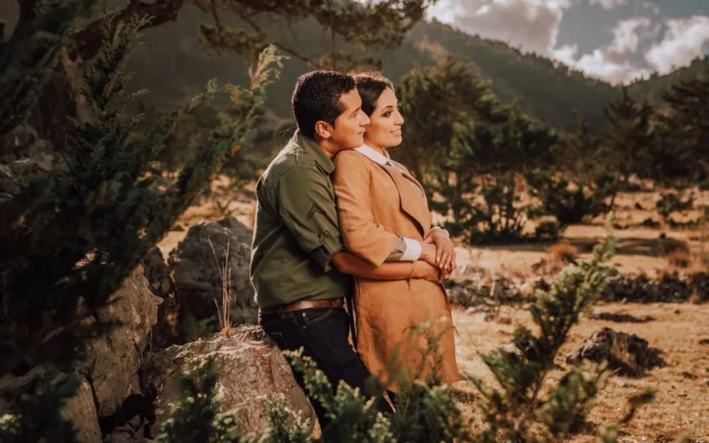 Couple embracing in an autumn landscape with warm sunlight.