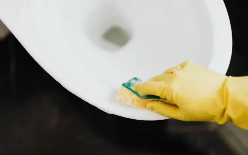 From above of crop unrecognizable person wearing yellow rubber gloves disinfecting and cleaning toilet bowl with sponge in bathroom