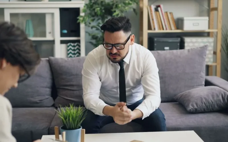 A stressed businessman in therapy session, showing visible emotions on a sofa.