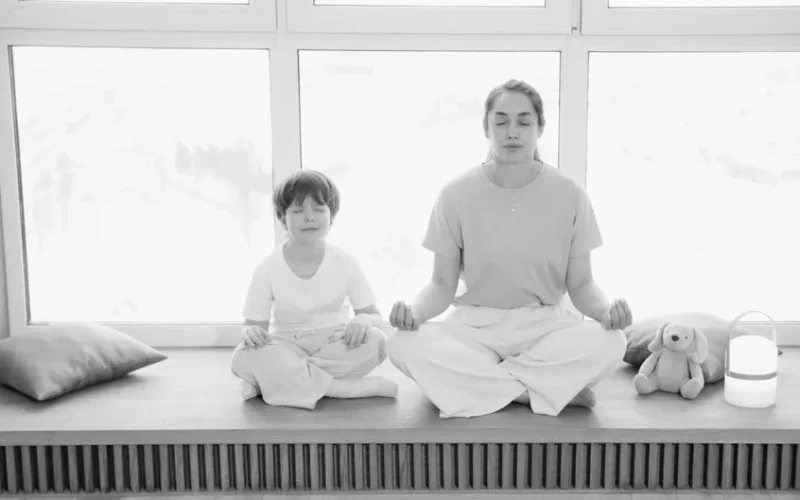 Mother and son practicing meditation, sharing a peaceful moment in a sunlit room.