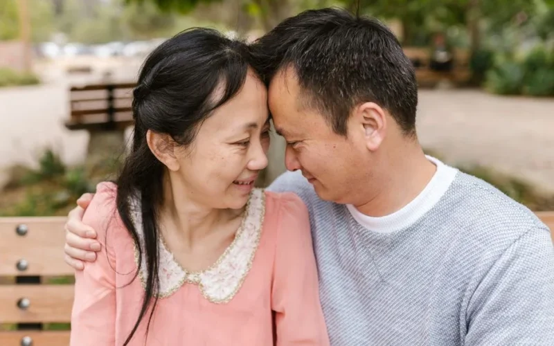 Smiling Asian couple embracing on a sunny day outdoors, sharing a moment of joy.