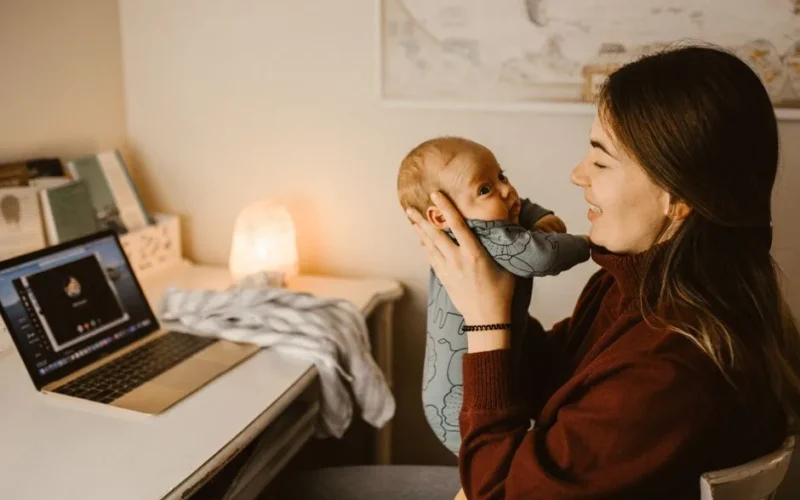 Mother holding baby while video calling from home office. Cozy and heartwarming indoor scene.