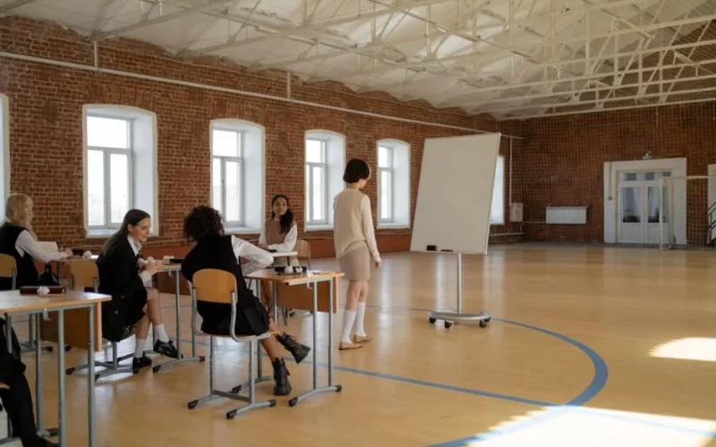 Students in school uniforms engaged in a lesson with a teacher in a spacious classroom.