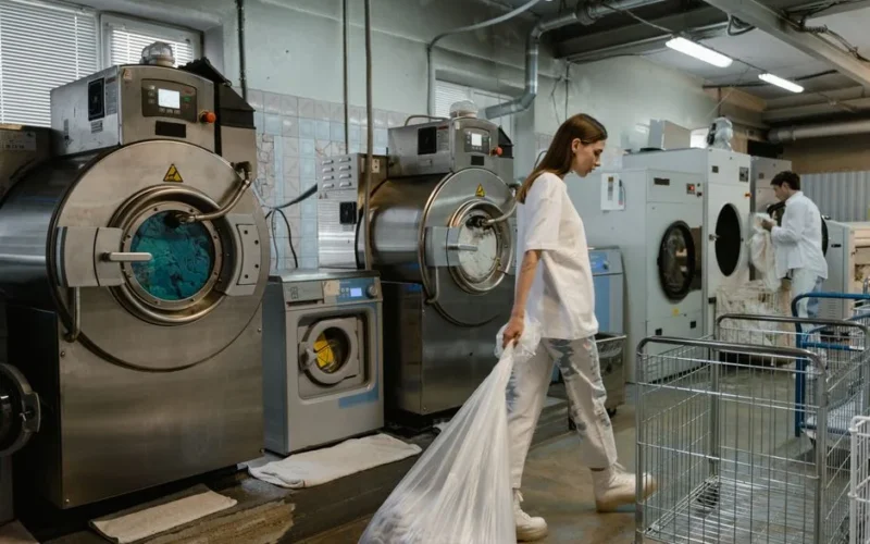 Busy industrial laundry with workers handling large washing machines.