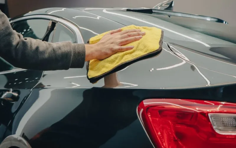 Close-up of hand polishing a shiny car with a yellow cloth indoors.