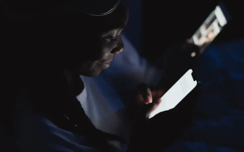 Close-up of a woman reading on her smartphone in a dark room, illuminated by the screen.