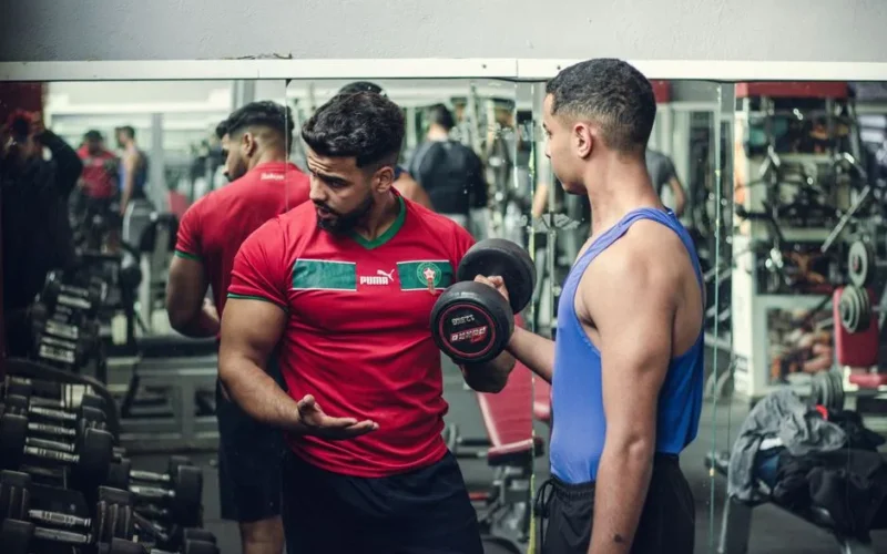 A fitness trainer guides a client in weight training at a well-equipped gym, emphasizing proper technique.