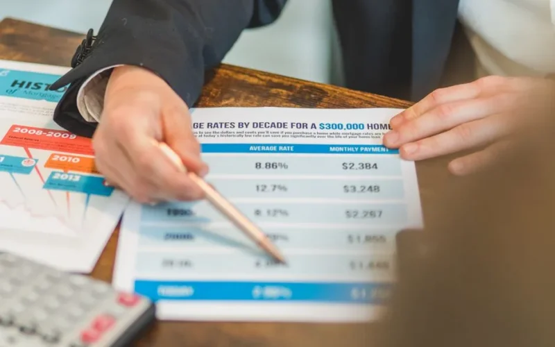 A close-up of hands analyzing mortgage rate documents with a pen and calculator in a business setting.