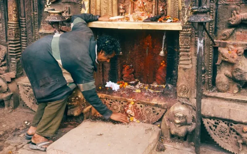 A man cleans a shrine at a richly carved traditional temple, embodying spirituality and culture.
