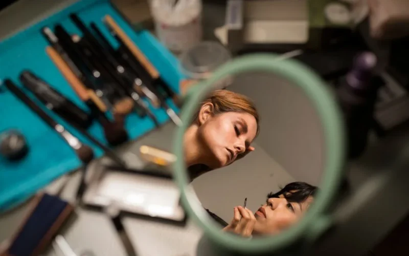 Makeup artist applying creative makeup, viewed through a mirror reflection.